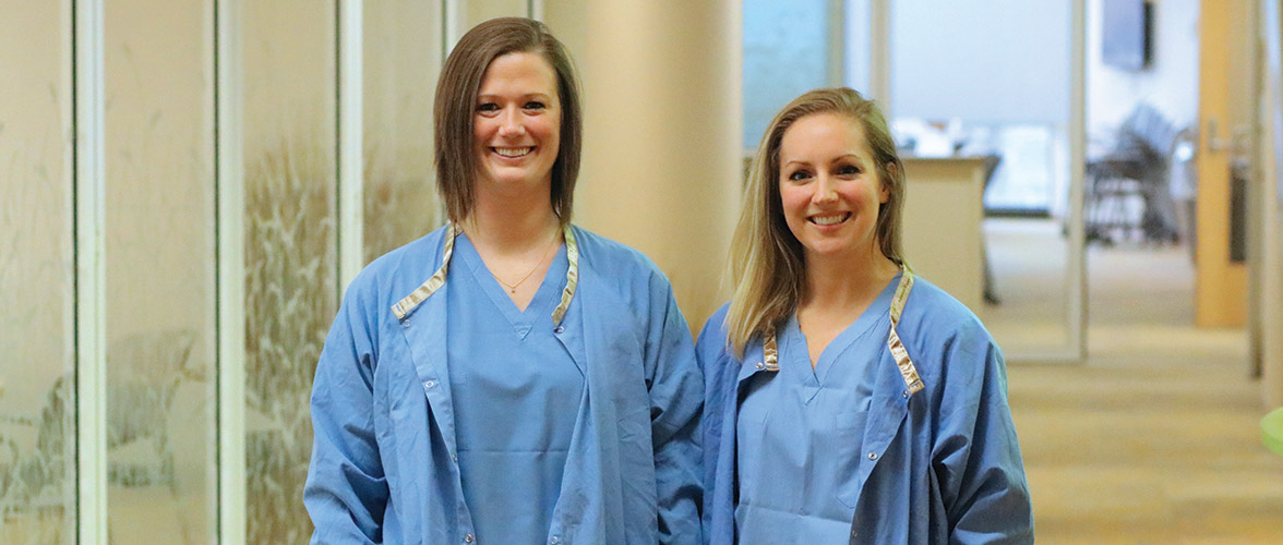 Halie Kauros and Kathryn Kopel dressed in scrubs in the hallway of the Bentson Center