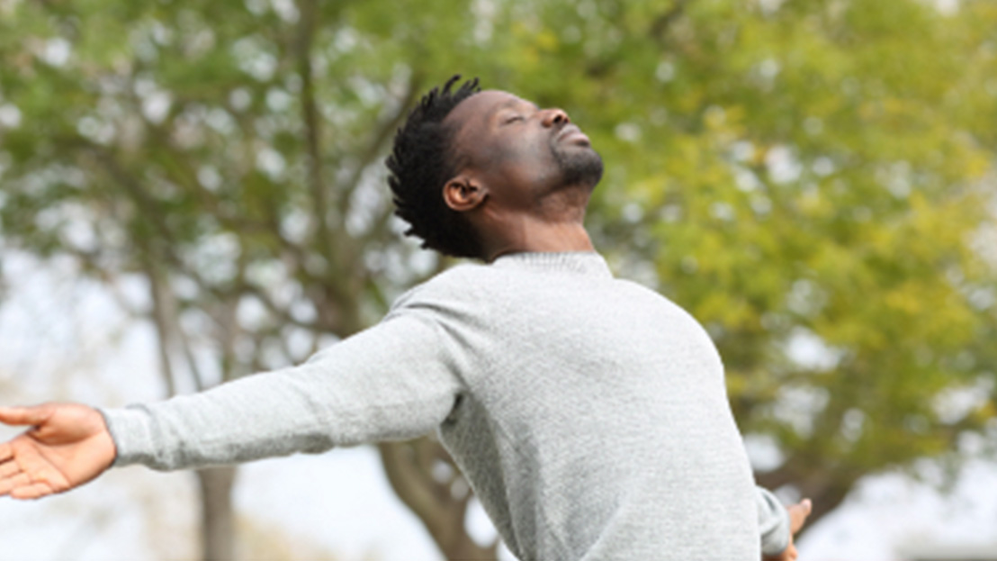 black male with arms outstretched and eyes closed in a park