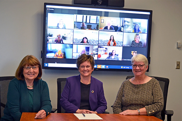 Christine Mueller, Connie Delaney and Diane Treat-Jacobson at a table with a zoom meeting on a screen behind them