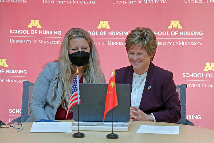 Carolyn Porta and Connie Delaney seated at a table behind the U.S. and China flags