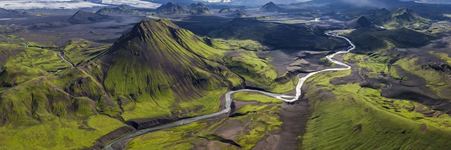 An aerial view of the rugged terrain of Iceland, featuring green mountains and winding rivers