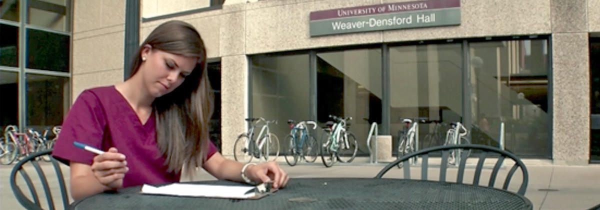 A Nursing student sitting outside Weaver Densford Hall filling out a scholarship application