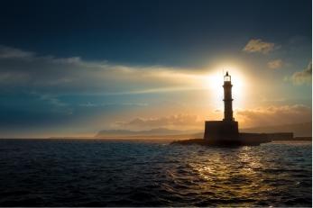 A lighthouse on the sea back-lit by a rising sun